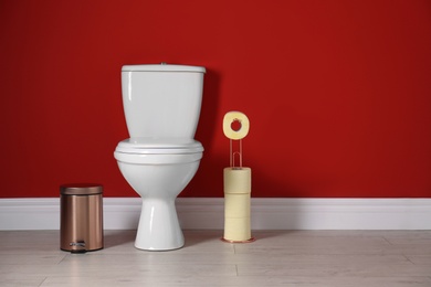 Toilet bowl with paper rolls and trash bin in restroom. Space for text