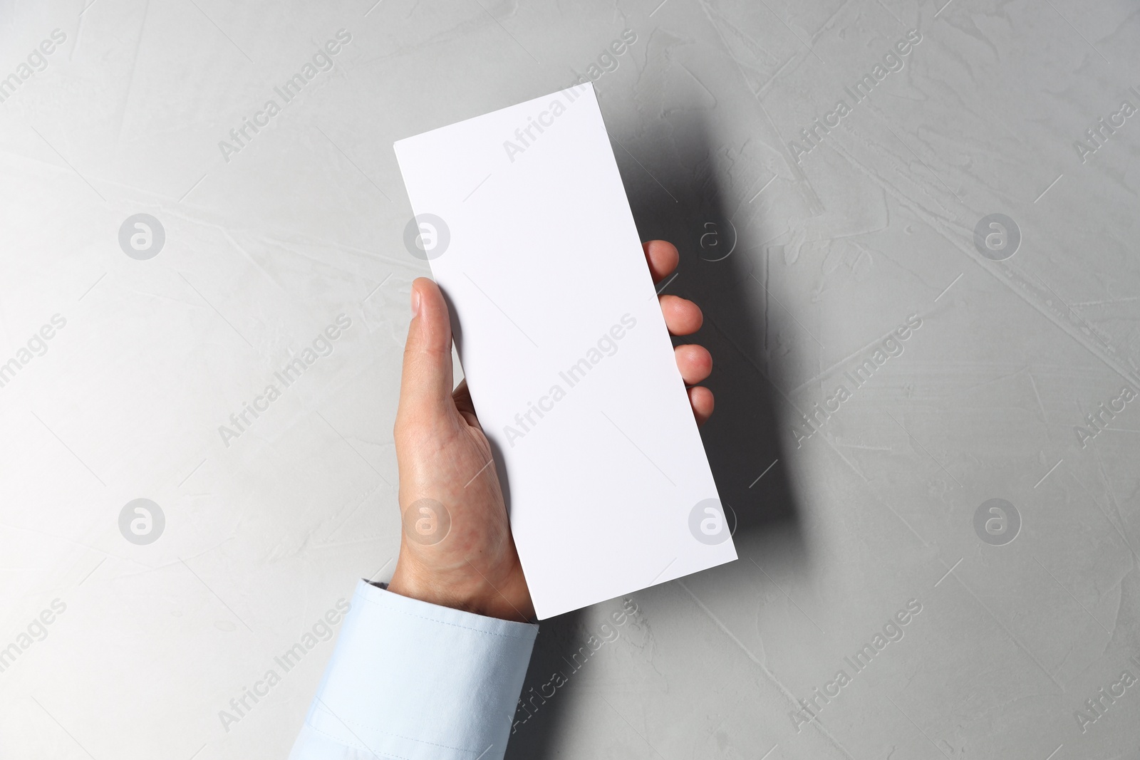 Photo of Man holding white blank card at light grey table, top view. Mockup for design