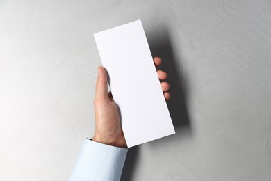 Photo of Man holding white blank card at light grey table, top view. Mockup for design