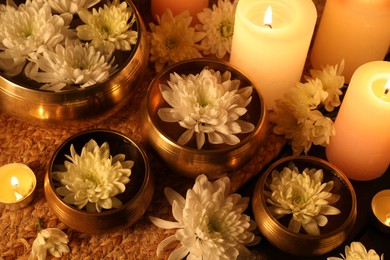 Photo of Tibetan singing bowls with water, beautiful flowers and burning candles on table, above view