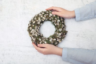 Woman holding wreath made of beautiful willow branches on light background, top view