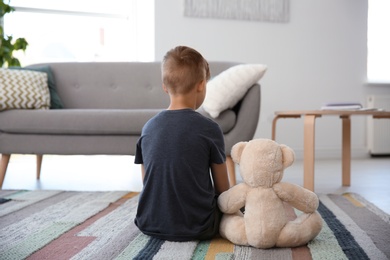 Photo of Lonely little boy with teddy bear sitting on floor at home. Autism concept