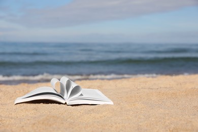 Photo of Open book on sandy beach near sea. Space for text