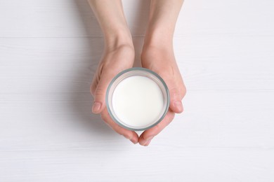 Photo of Woman holding glass of milk at white wooden table, top view