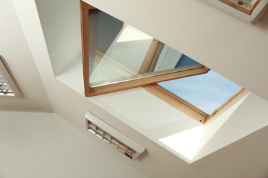 Photo of Open skylight roof window on slanted ceiling in attic room, low angle view