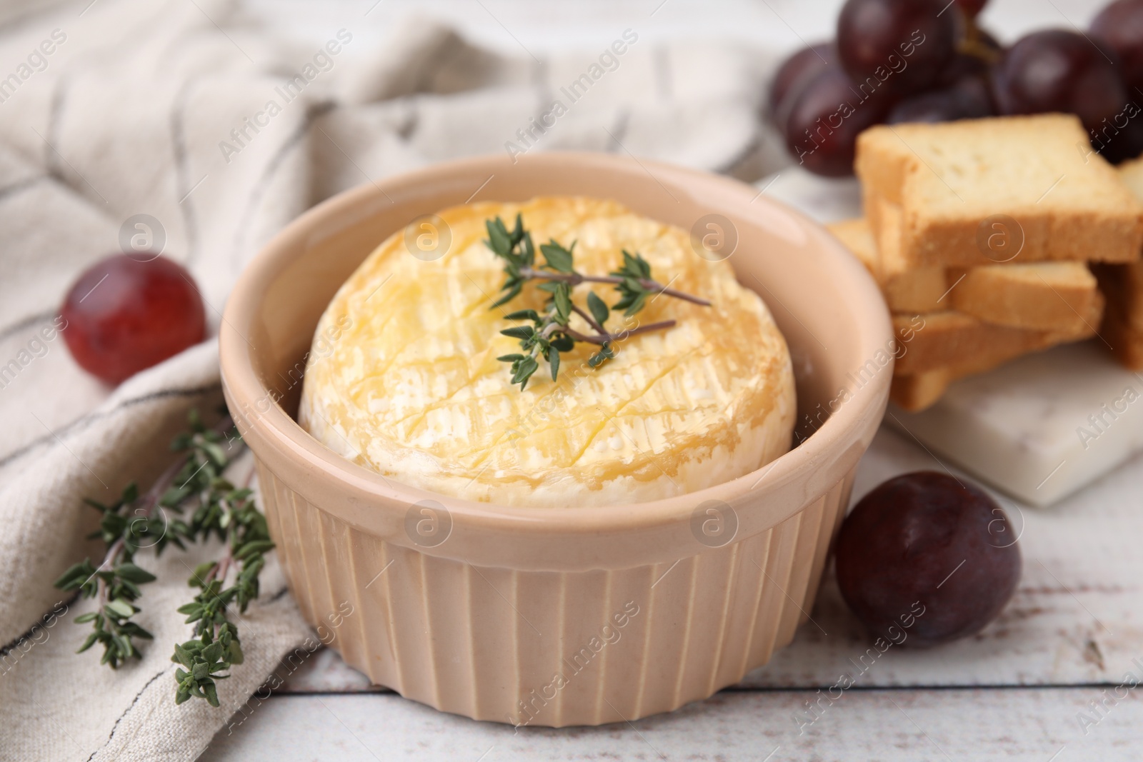 Photo of Tasty baked camembert in bowl, thyme, grapes and croutons on wooden table, closeup