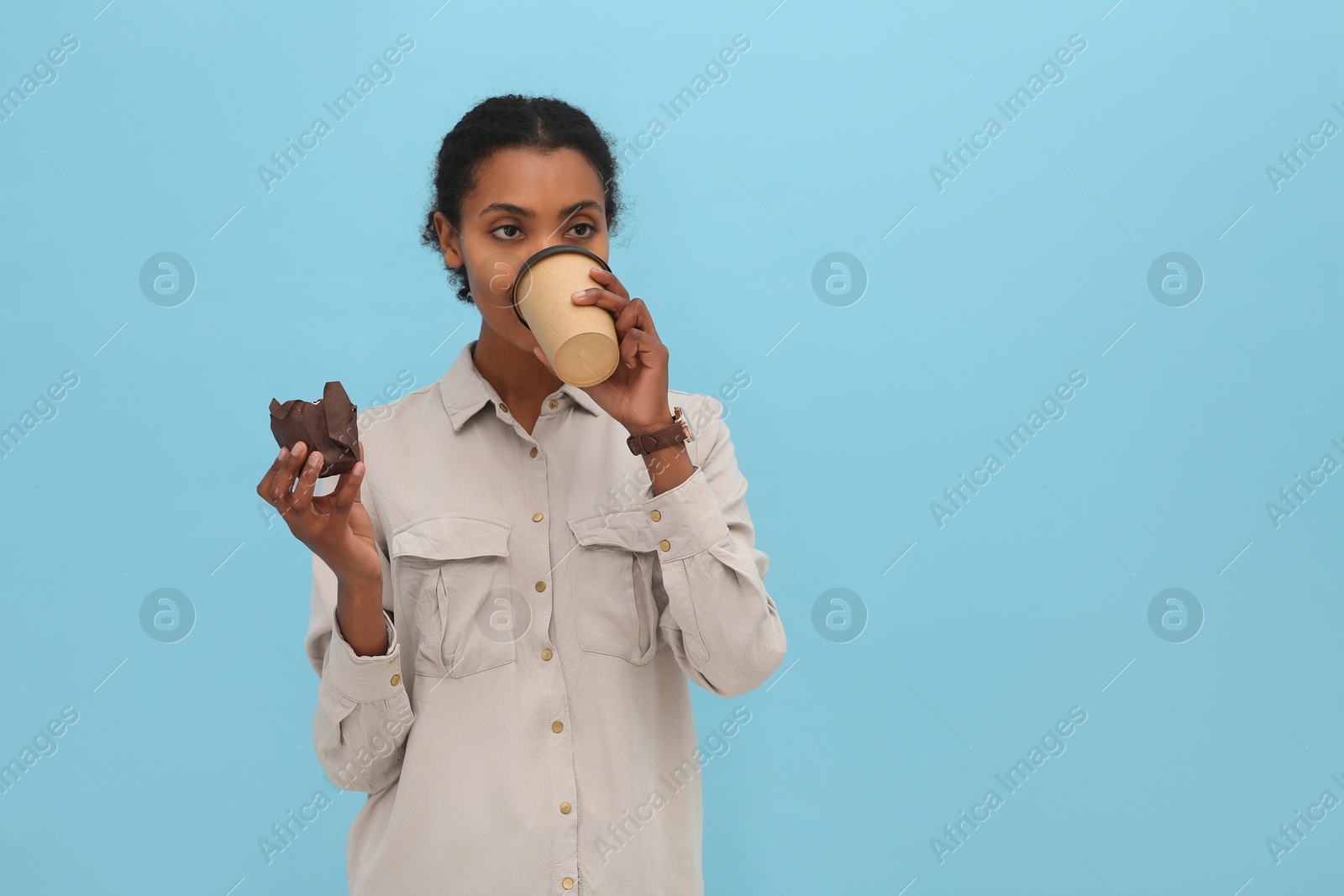 Photo of African American intern with cupcake drinking coffee on light blue background. Space for text