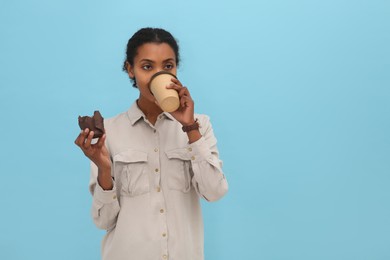 Photo of African American intern with cupcake drinking coffee on light blue background. Space for text