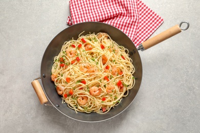 Photo of Frying pan with spaghetti and shrimps on light background, top view