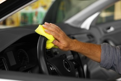 Man cleaning steering wheel with rag in car, closeup