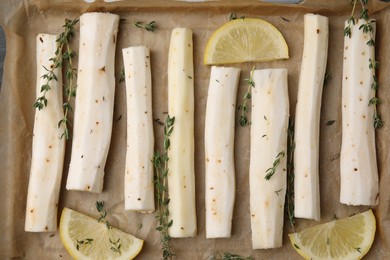 Photo of Baking tray with raw salsify roots, lemon and thyme as background, top view