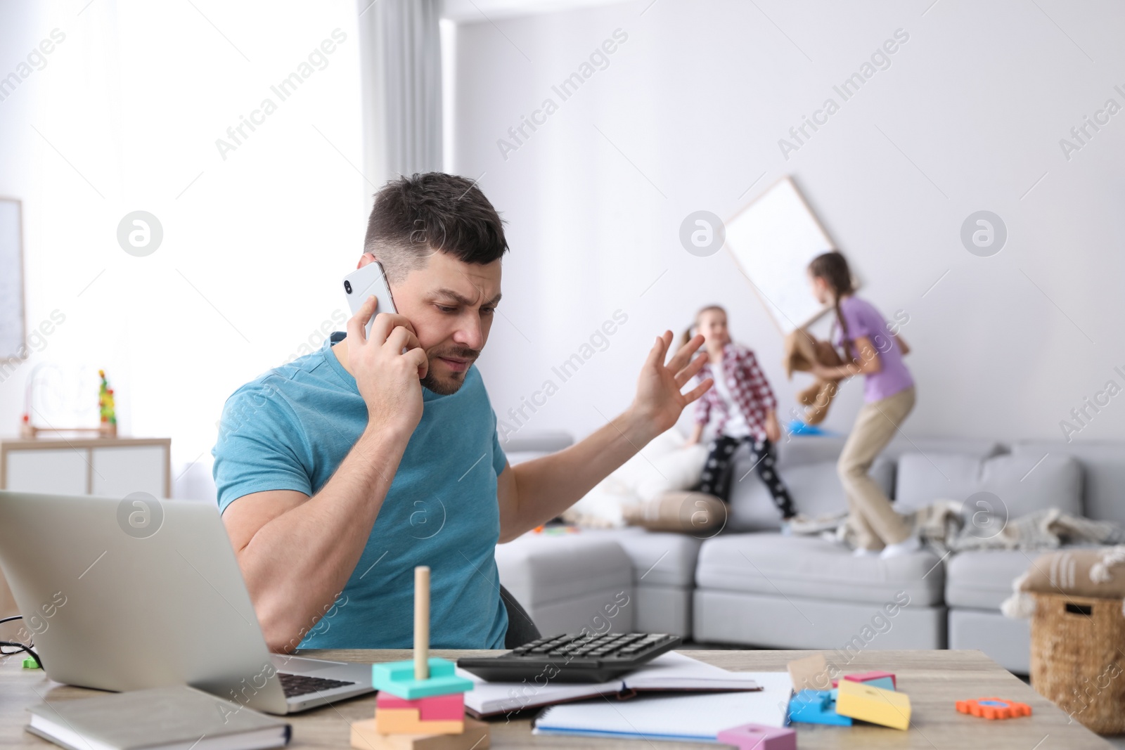 Photo of Children disturbing stressed man in living room. Working from home during quarantine