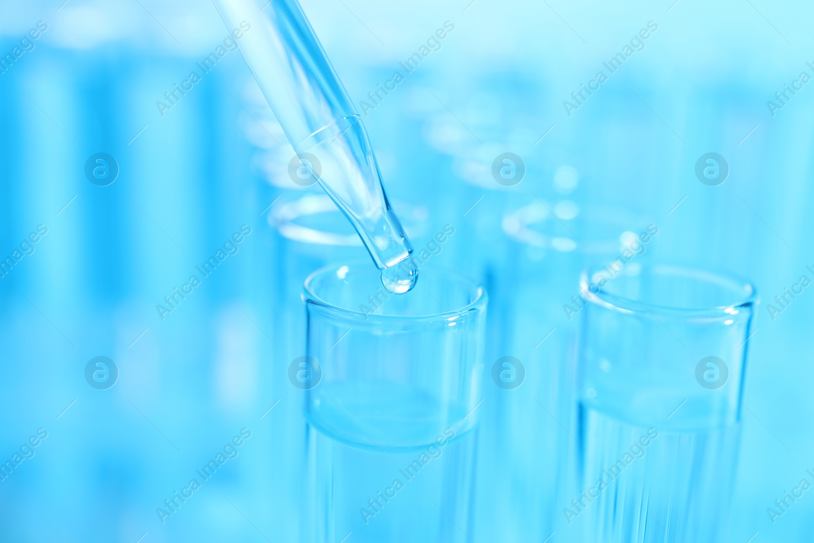 Photo of Dripping liquid from pipette into test tube on light blue background, closeup