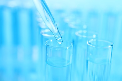 Dripping liquid from pipette into test tube on light blue background, closeup