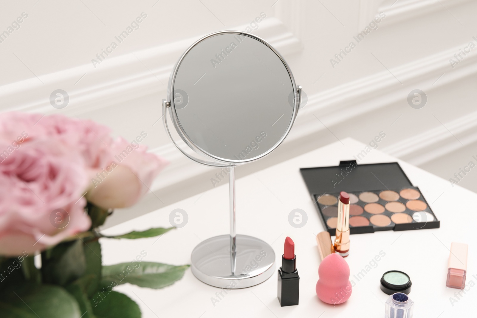 Photo of Mirror, cosmetic products and pink roses on white dressing table, closeup