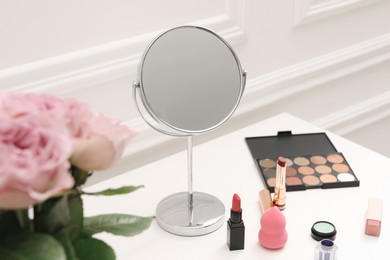 Mirror, cosmetic products and pink roses on white dressing table, closeup