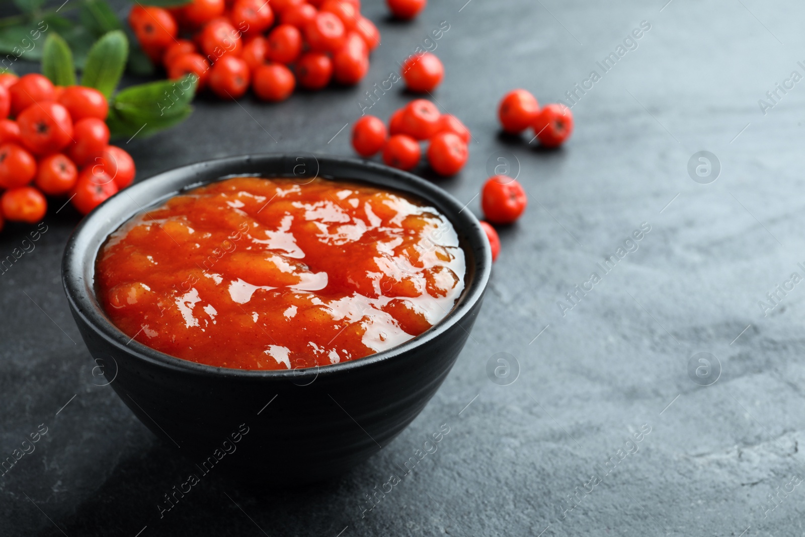 Photo of Delicious rowan jam in bowl on dark table. Space for text