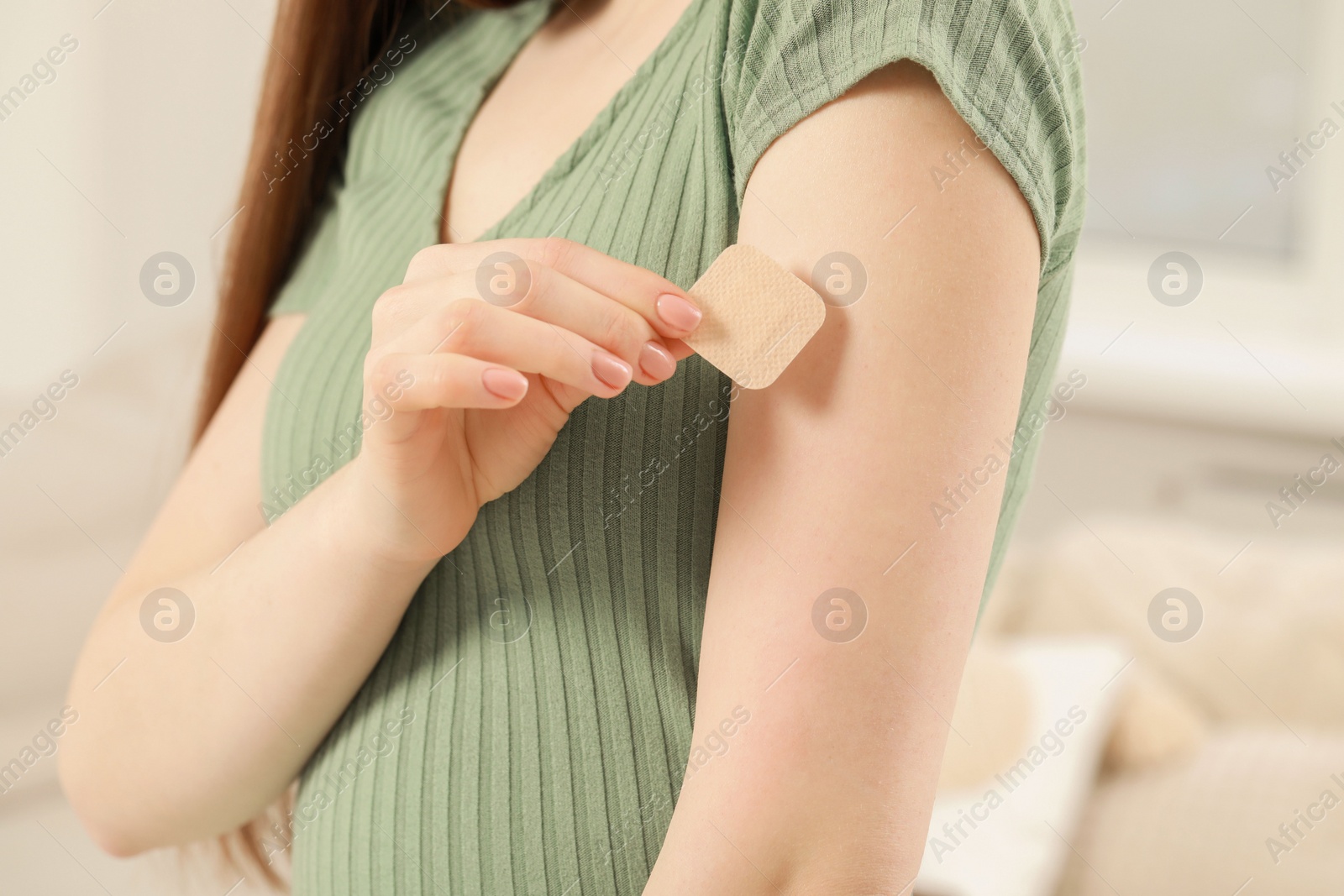 Photo of Woman applying contraceptive patch onto her arm indoors, closeup