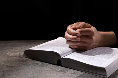 Photo of Religion. Christian woman praying over Bible at table against black background, closeup. Space for text