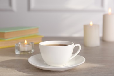 Cup of aromatic coffee and burning candles on wooden table indoors