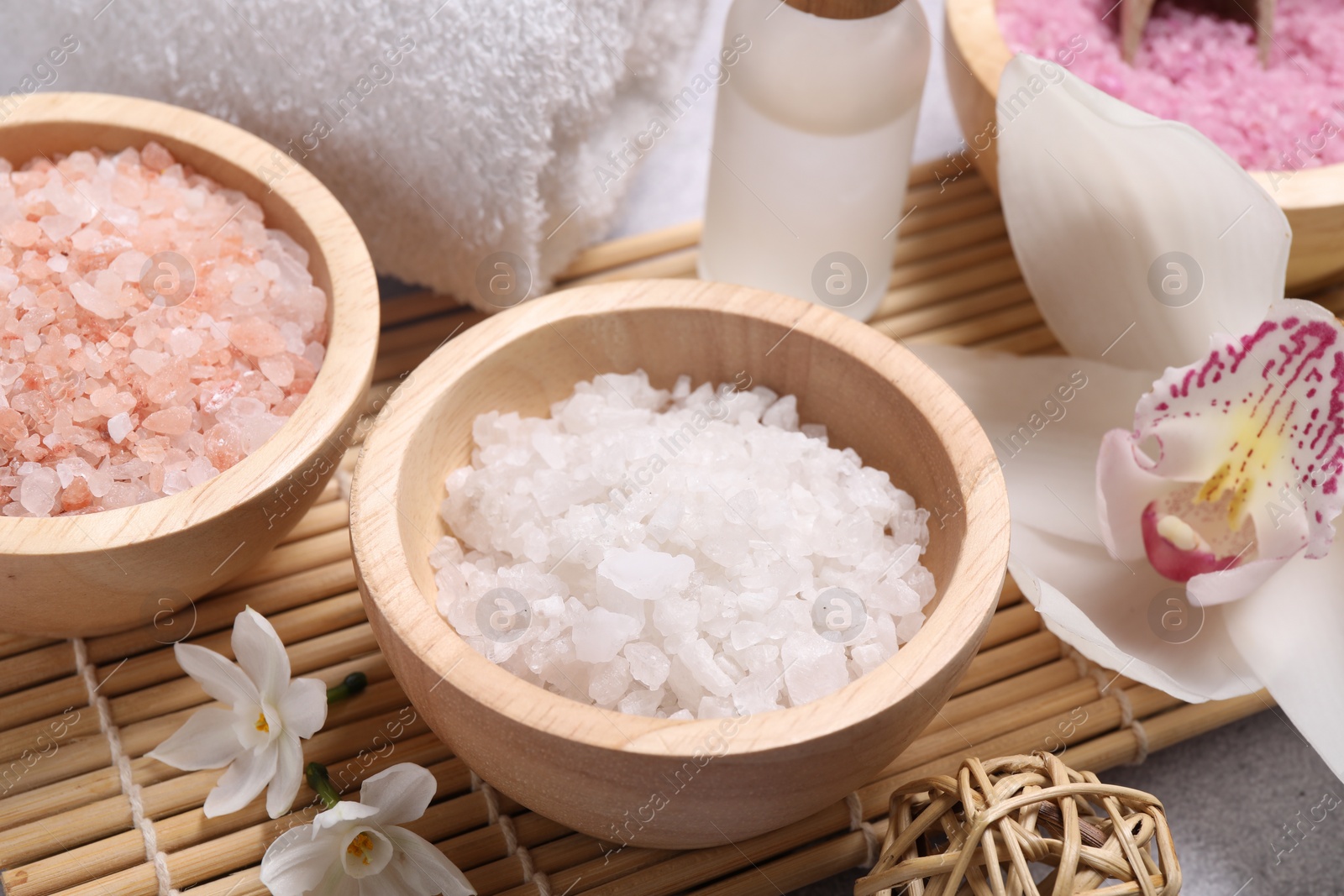 Photo of Different types of sea salt and flowers on light table, closeup. Spa products