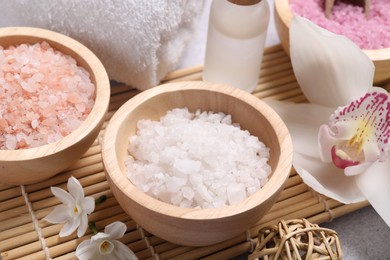 Different types of sea salt and flowers on light table, closeup. Spa products