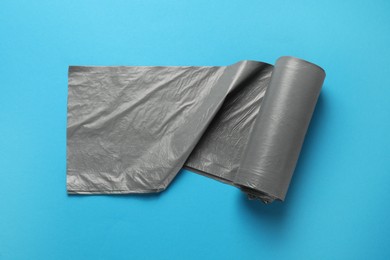 Photo of Roll of grey garbage bags on light blue background, top view. Cleaning supplies