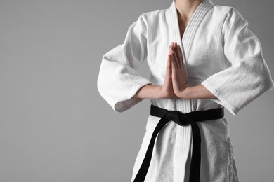 Photo of Martial arts master in keikogi with black belt on grey background, closeup. Space for text