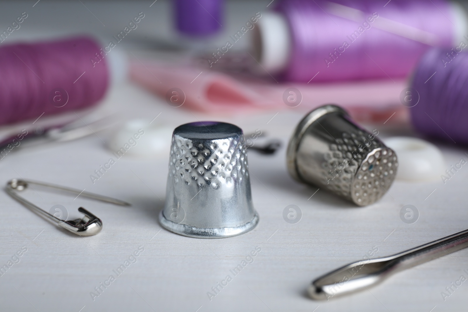 Photo of Silver thimbles near sewing tools on white wooden table