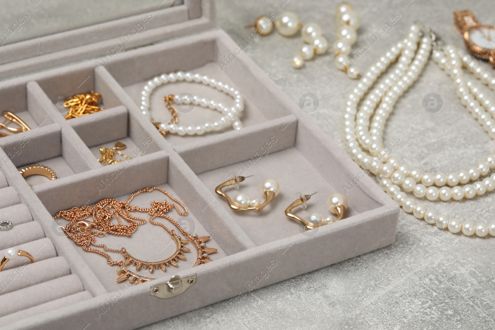 Photo of Jewelry box with many different accessories on light grey table, closeup