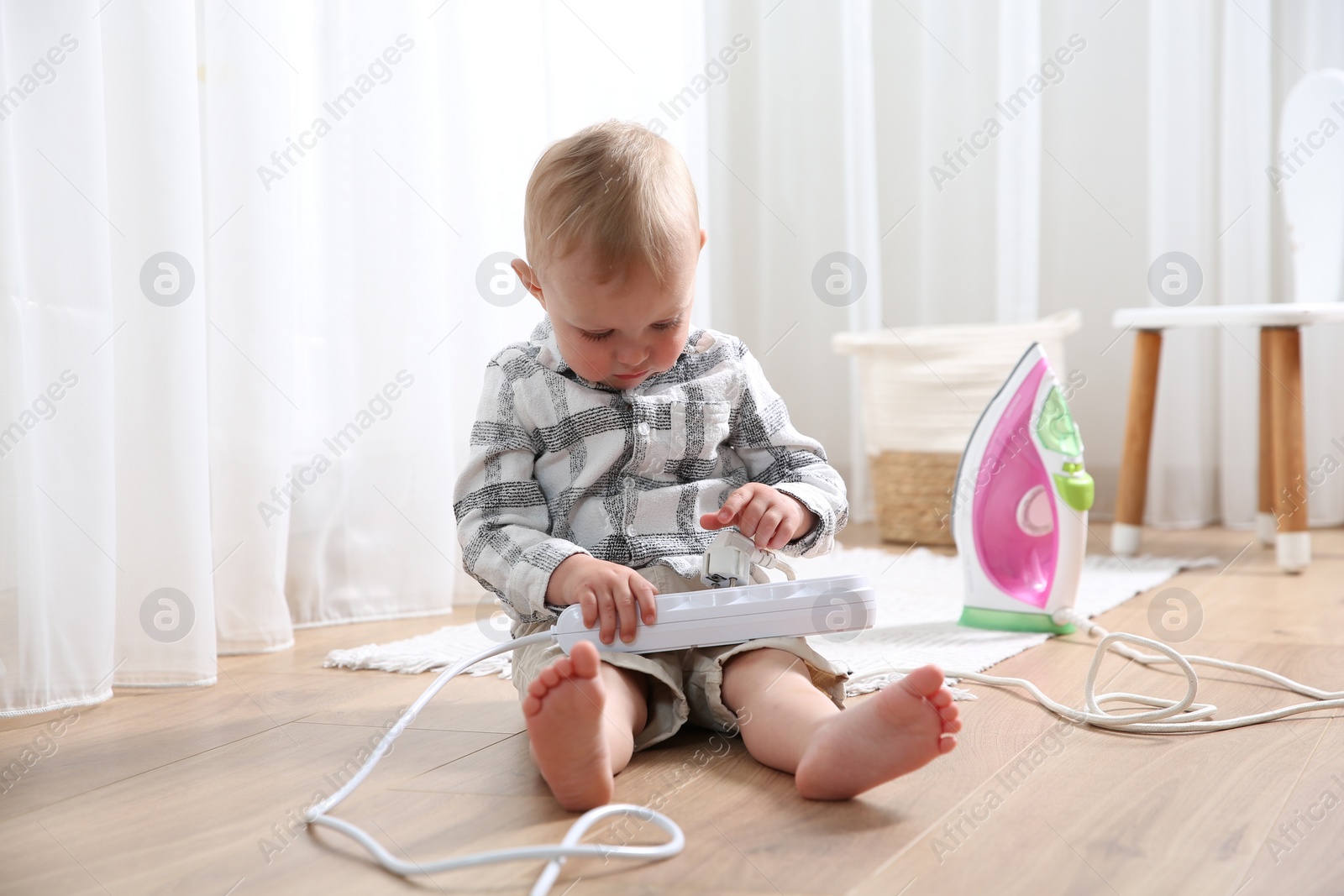 Photo of Little child playing with power strip and iron plug on floor at home. Dangerous situation