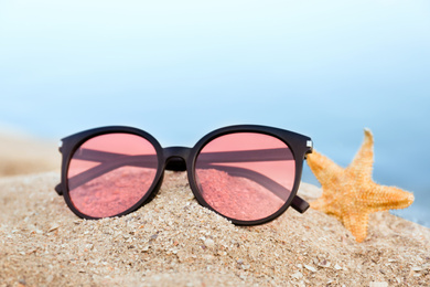 Photo of Stylish sunglasses and starfish on sandy beach, closeup