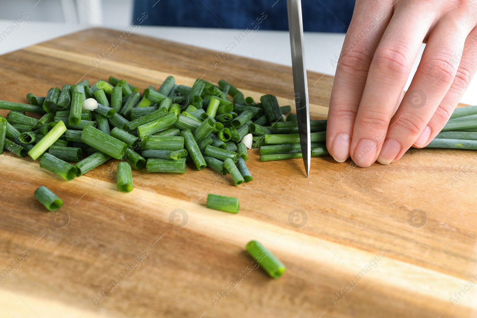 Photo of Woman cutting green spring onion on wooden board, closeup