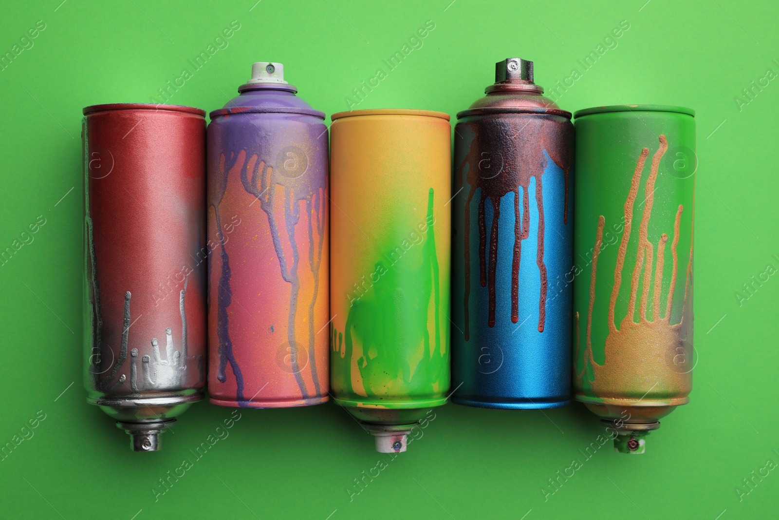 Photo of Used cans of spray paints on green background, flat lay. Graffiti supplies