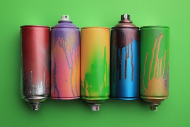 Used cans of spray paints on green background, flat lay. Graffiti supplies