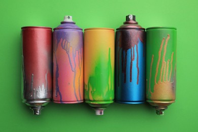 Photo of Used cans of spray paints on green background, flat lay. Graffiti supplies