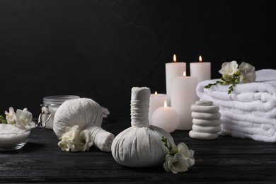 Photo of Herbal massage bags, candles, folded towels spa and stones on black wooden table