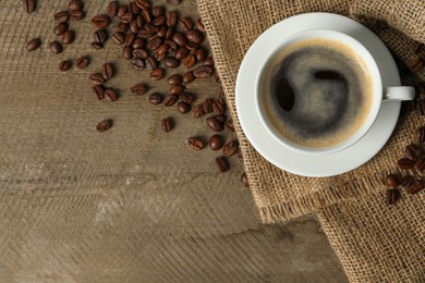 Photo of Cup of aromatic coffee and beans on wooden table, flat lay. Space for text