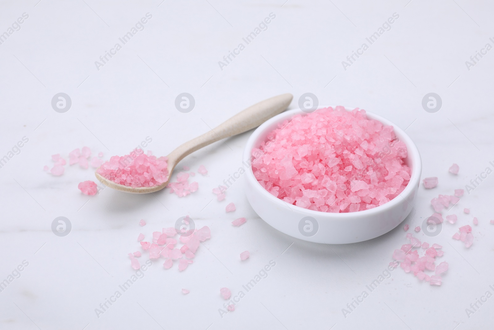 Photo of Plate and spoon with pink sea salt on white marble table