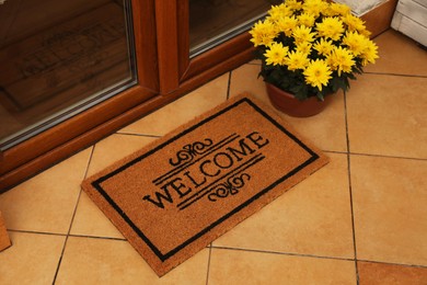 Photo of Door mat with word Welcome and beautiful flowers on floor near entrance