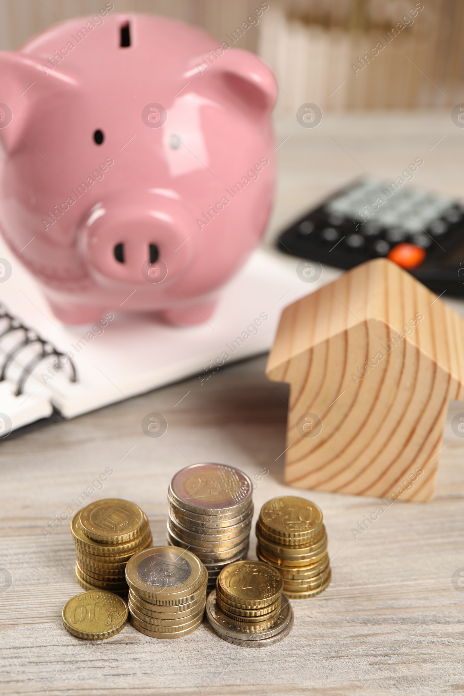 Photo of House model, piggy bank, stacked coins, notebook and calculator on wooden table, selective focus