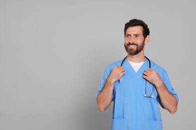 Photo of Happy doctor with stethoscope on light grey background. Space for text