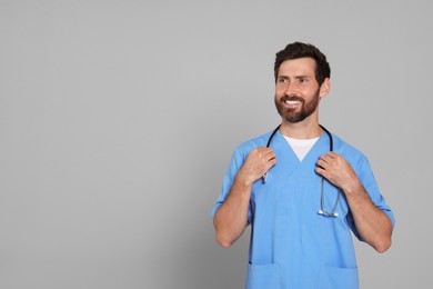 Happy doctor with stethoscope on light grey background. Space for text