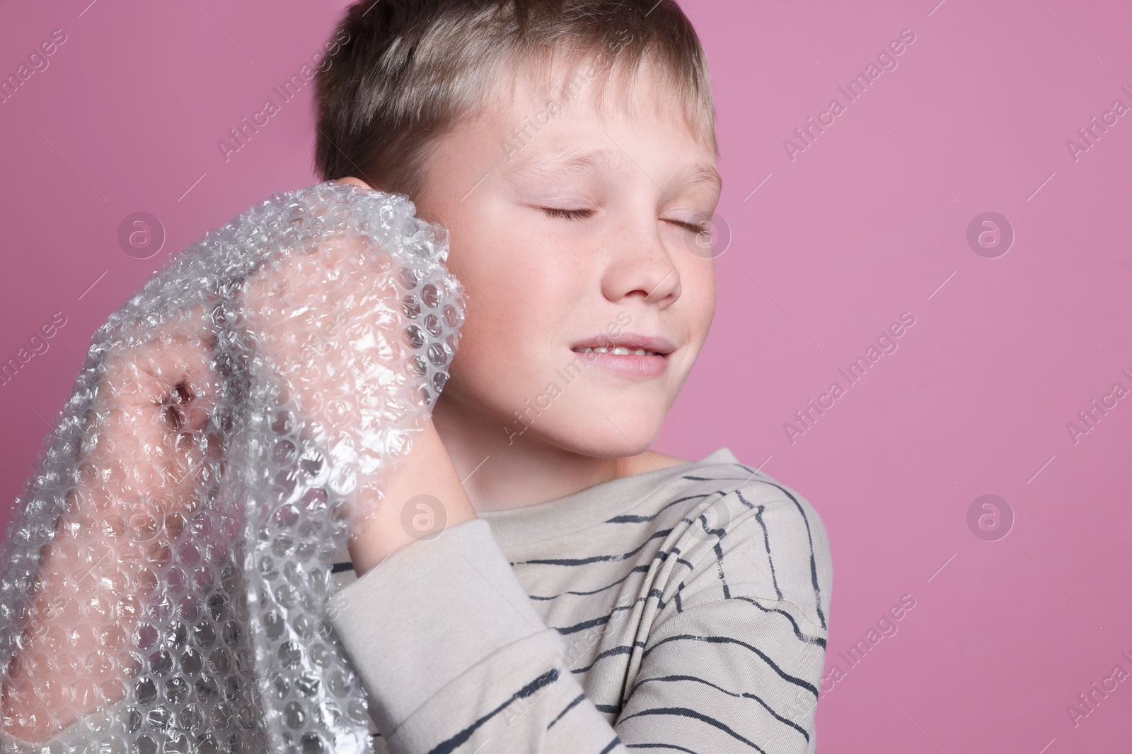 Photo of Boy popping bubble wrap on pink background, closeup. Stress relief