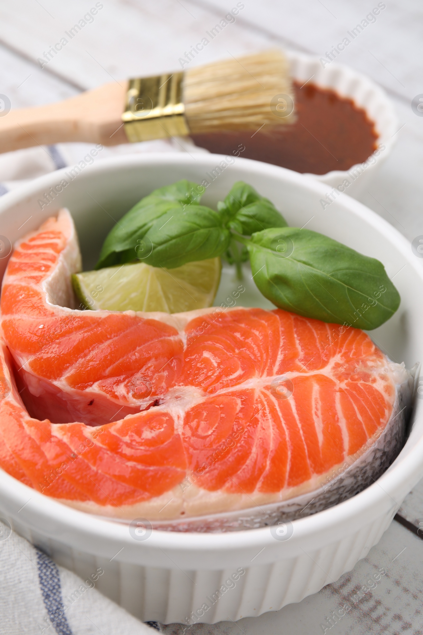 Photo of Fresh marinated fish, brush and lime on white wooden table, closeup