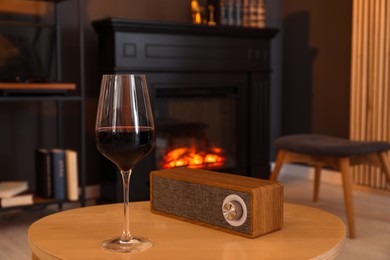 Photo of Glass of red wine and portable speaker on table in room. Relax at home