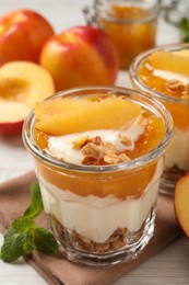Photo of Tasty peach yogurt with granola, pieces of fruit and jam on table
