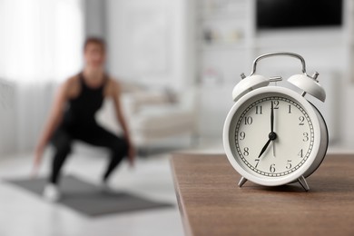 Photo of Morning routine. Alarm clock on wooden table and woman doing exercise, selective focus. Space for text