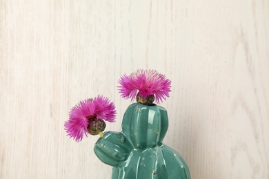 Photo of Trendy cactus shaped ceramic vase with flowers on wooden background