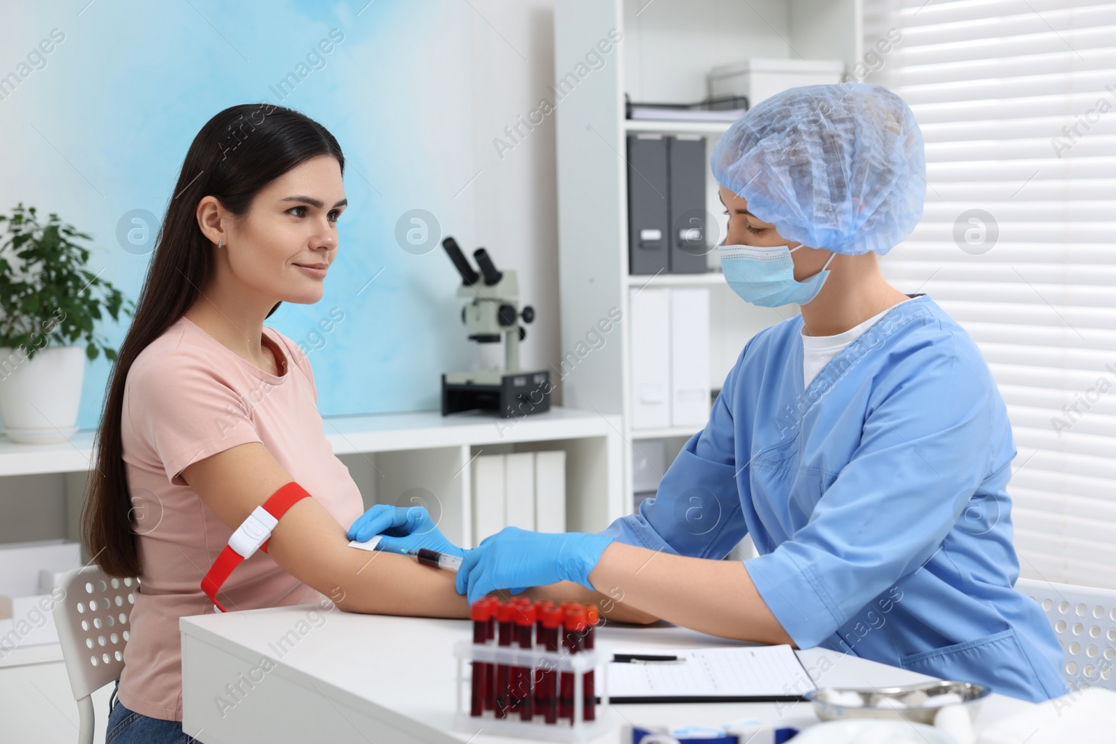 Photo of Laboratory testing. Doctor taking blood sample from patient at white table in hospital